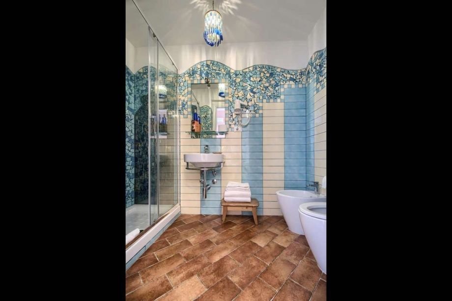 Artistic bathroom design featuring blue and light blue mosaic walls and a large glass shower in the studio apartment.